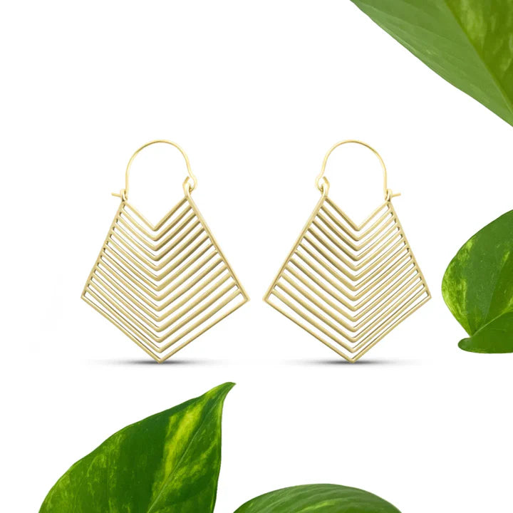 Golden geometric hoop earrings displayed on white surface with green leaves, bold art deco design.