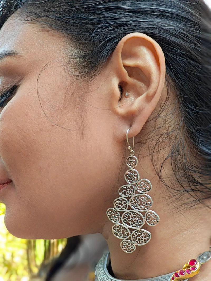 Close-up of model wearing silver statement earrings, featuring intricate handcrafted design with modern bohemian flair.