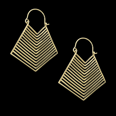 Brass gold geometric earrings placed beside pink flower on dark background, highlighting contrast and modern artistry.