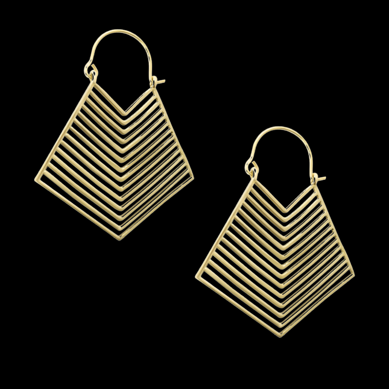 Brass gold geometric earrings placed beside pink flower on dark background, highlighting contrast and modern artistry.