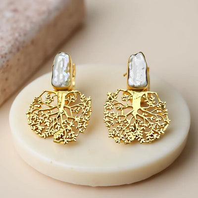 Gold handmade tree-shaped statement studs with baroque pearls displayed on cream stand, featuring intricate nature-inspired detailing.