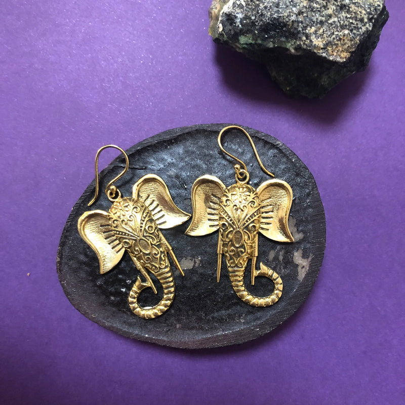 Gold elephant Ganesh earrings placed on black round plate with purple background, highlighting detailed craftsmanship and spiritual design.