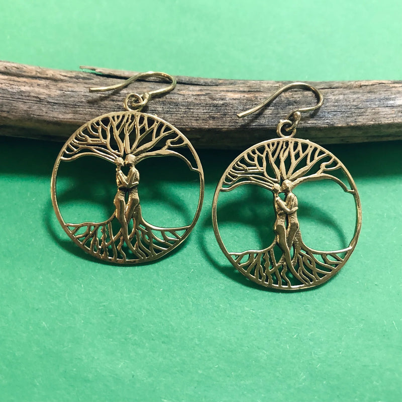 Gold Lovers Tree of Life earrings hanging on wooden branch with green background, highlighting artistic and symbolic craftsmanship.