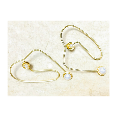 Contemporary gold wire earrings with white freshwater pearls displayed on beige background, featuring abstract open design and minimal elegance.