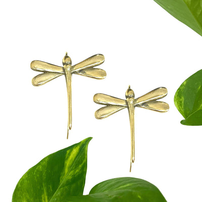 Gold-plated dragonfly earrings placed with green leaves, reflecting organic design and refined elegance.