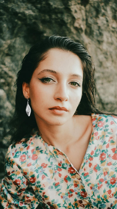 Woman wearing sterling silver leaf drop earrings against a wall
