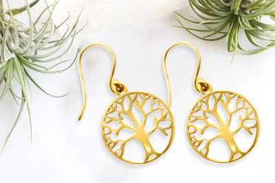 Flat lay of gold tree of life earrings on marble surface with natural decor.