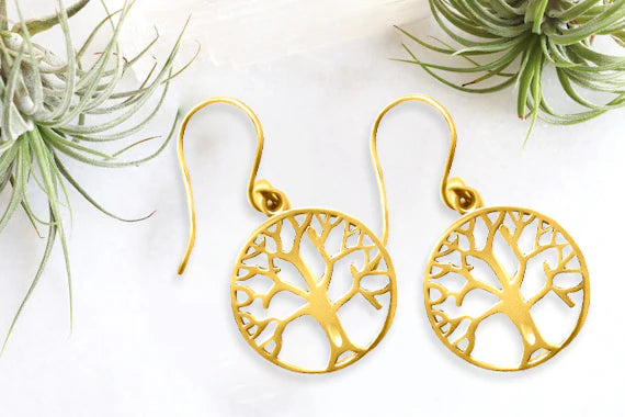 Flat lay of gold tree of life earrings on marble surface with natural decor.
