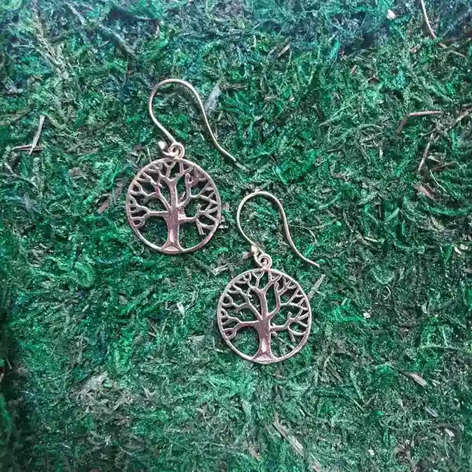 Gold tree of life earrings placed on green grass background, nature-inspired design.