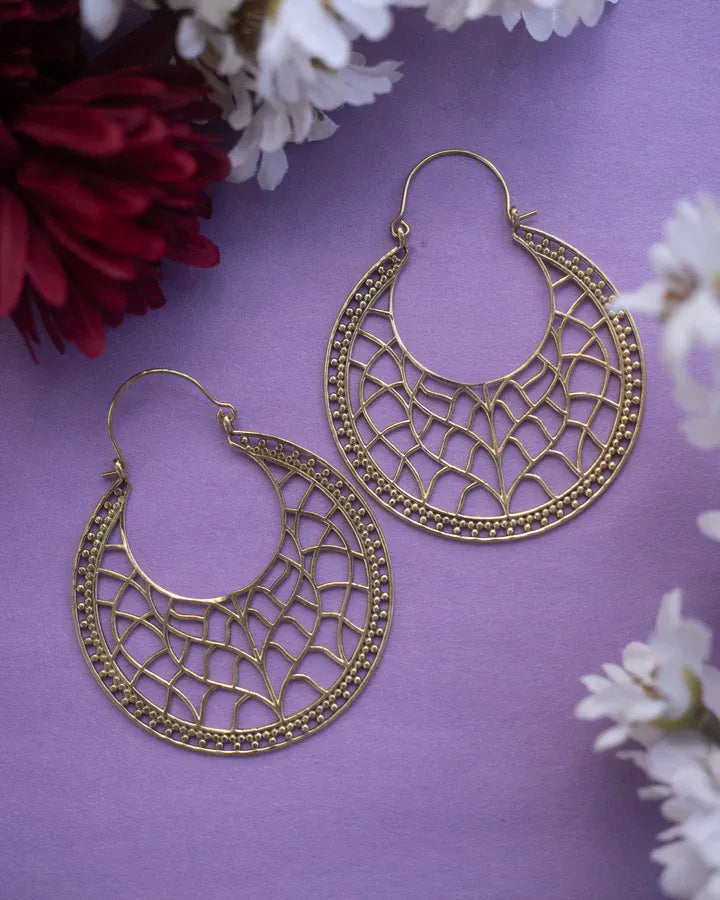 Big gold jali drop hoop earrings displayed on purple surface with flower accents.