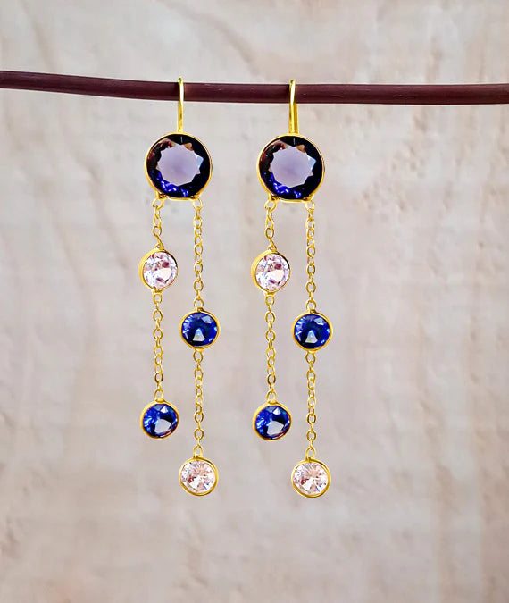 Pair of blue crystal drop earrings hanging on fabric background, contemporary statement style.
