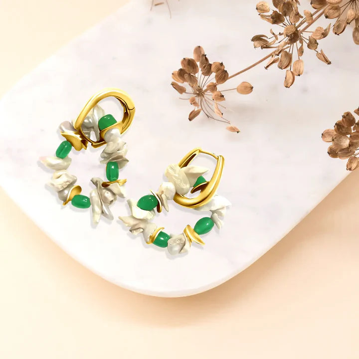 Flat lay of emerald pearl cluster hoop earrings on marble background, delicate statement jewelry.