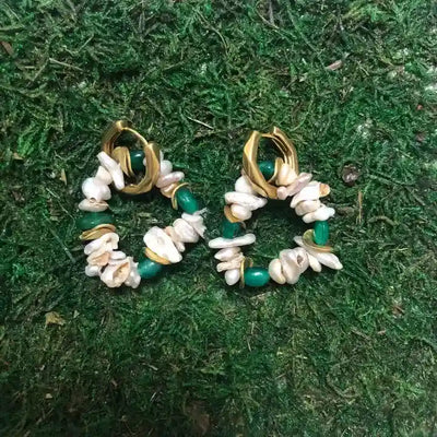 Emerald and pearl cluster hoop earrings placed on green grass background, gold-plated finish.
