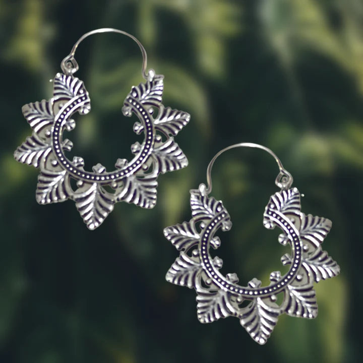 Lifestyle photo of silver Evergreen Creole Leaf earrings hanging on green natural background.