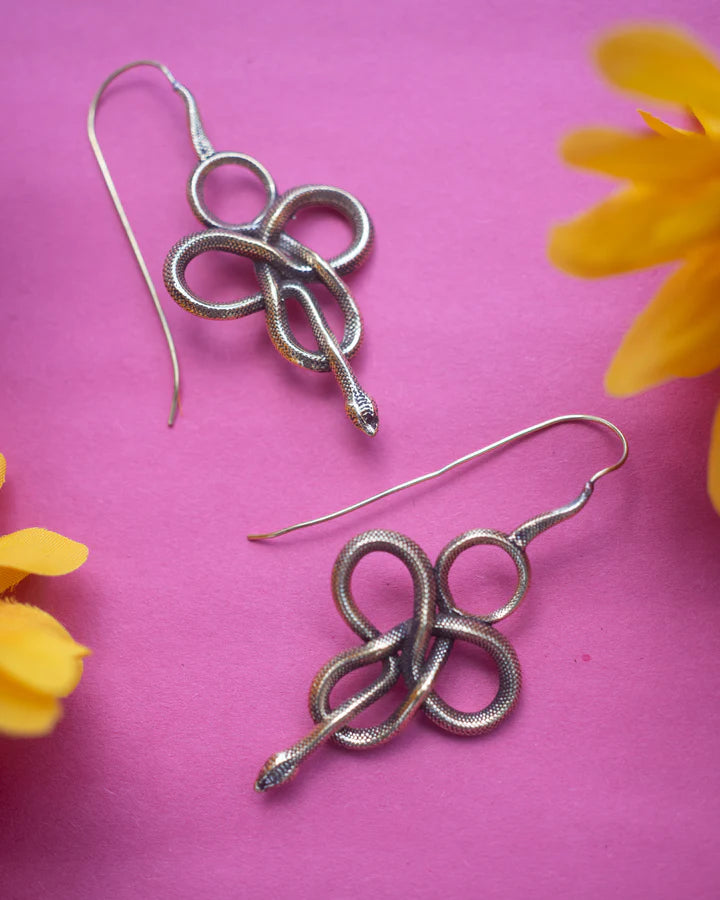 Flat lay of snake Viking Nordic tribal gold plated drop dangle earrings on purple floral background.