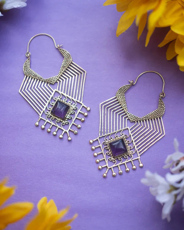 Flatlay of geometric purple labradorite beaded earrings with floral accents on purple background.