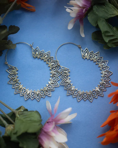 Flat lay of Mandala Flower Extra Large Hoop Earrings placed on blue background with flowers.