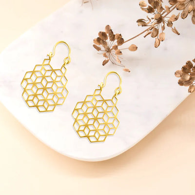 Flat lay of honeycomb-inspired gold drop earrings on marble surface, contemporary chic look.