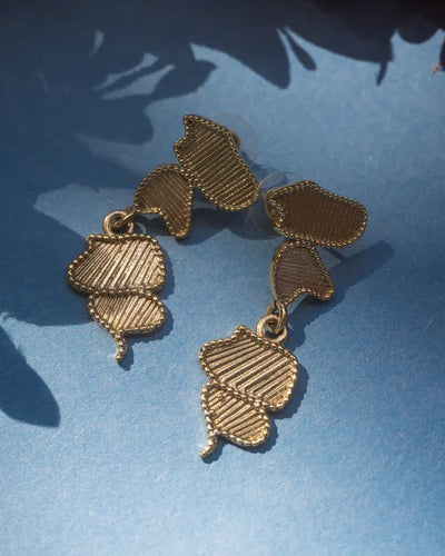 Flat lay of gold asymmetrical stud earrings on blue background, stylish statement design.