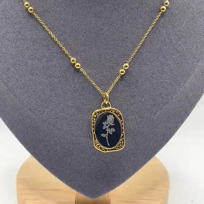 Black enamel floral pendant necklace with gold frame and floral detailing, sophisticated minimal design.