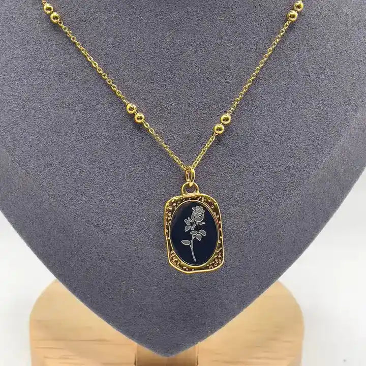 Black enamel floral pendant necklace with gold frame and floral detailing, sophisticated minimal design.