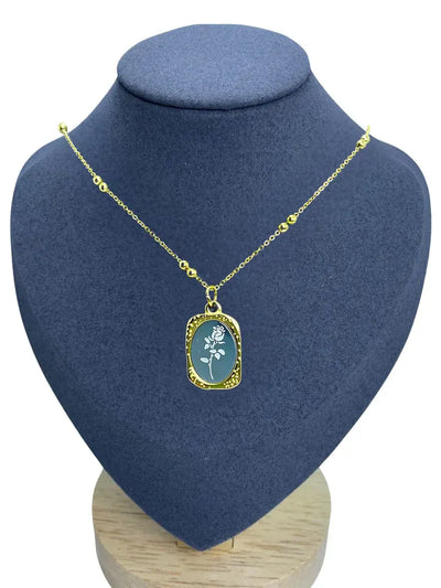 Gold enamel floral pendant necklace displayed on grey bust stand, elegant oval charm design.