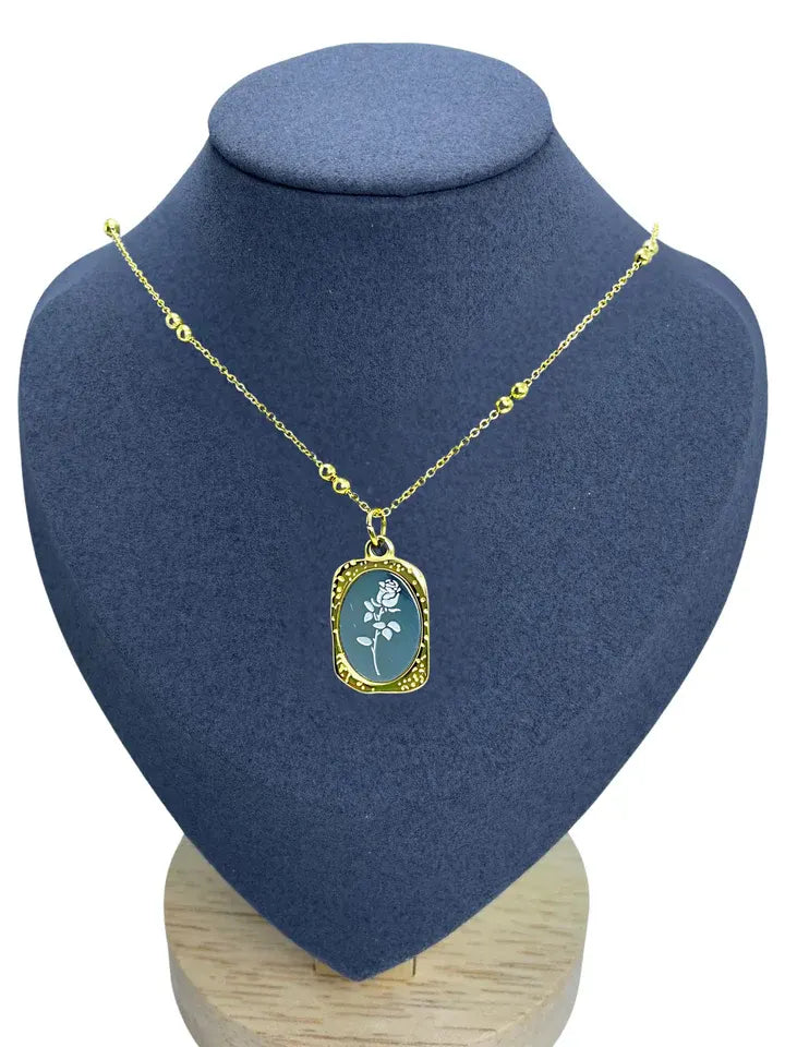Gold enamel floral pendant necklace displayed on grey bust stand, elegant oval charm design.