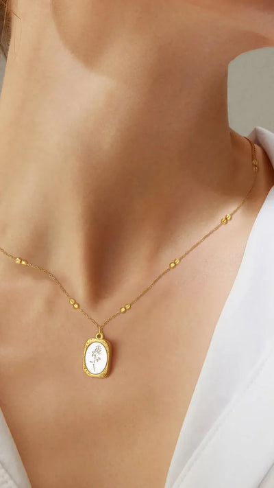 Model wearing gold enamel floral pendant necklace, delicate and elegant accessory.