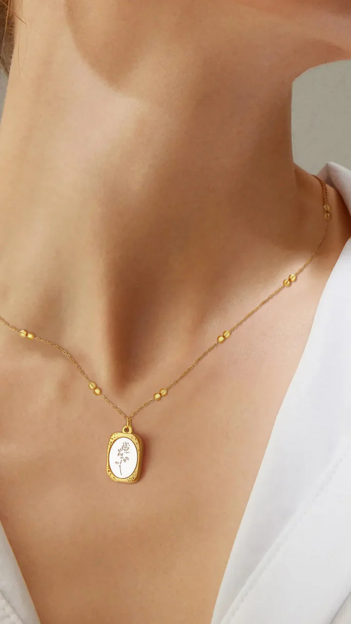Model wearing gold enamel floral pendant necklace, delicate and elegant accessory.