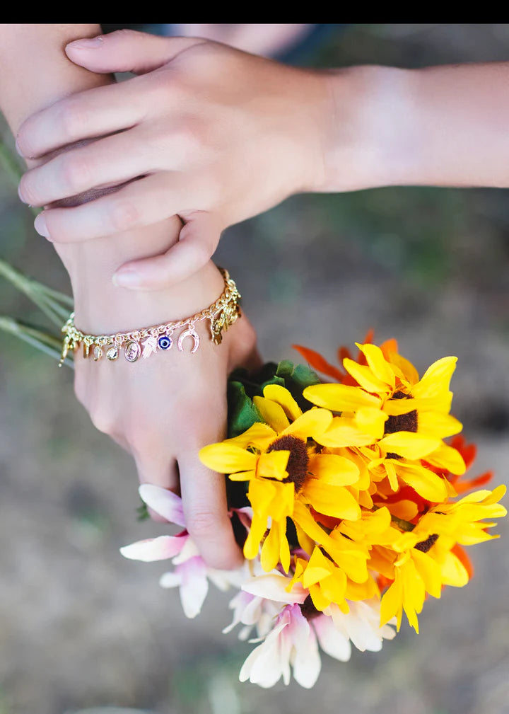 Gold evil eye charm bracelet styled on hand with floral accents for boho-inspired fashion.