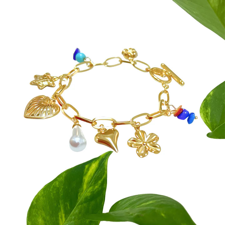 Gold charm bracelet with colorful beads and charms displayed on green leaf background, modern chic accessory.