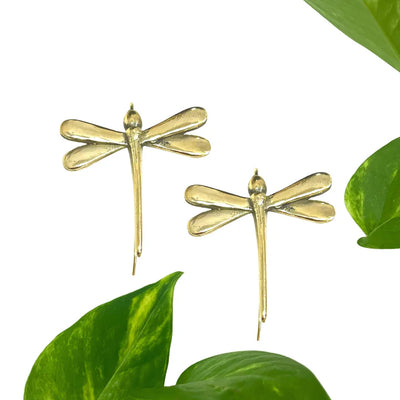 Flat lay of golden dragonfly earrings with green leaves, eco-inspired modern accessory.