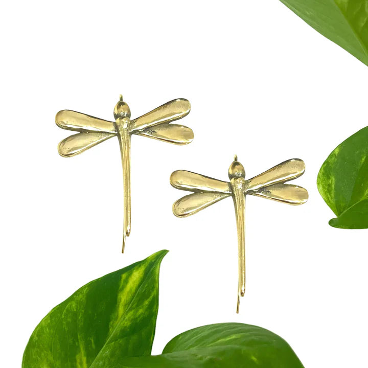 Flat lay of golden dragonfly earrings with green leaves, eco-inspired modern accessory.