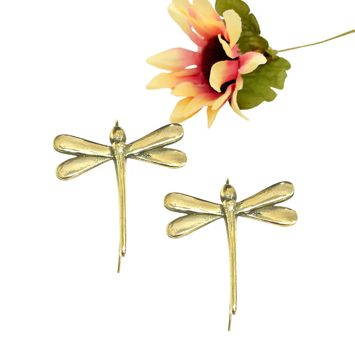 Golden dragonfly earrings displayed beside flower, elegant botanical jewelry style.