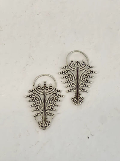 Golden filigree earrings laid flat on textured surface, intricate handcrafted jewelry design.