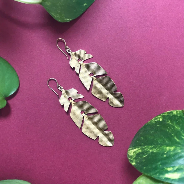 Flat lay of golden leaf drop earrings on magenta background with leaves, artistic boho design.