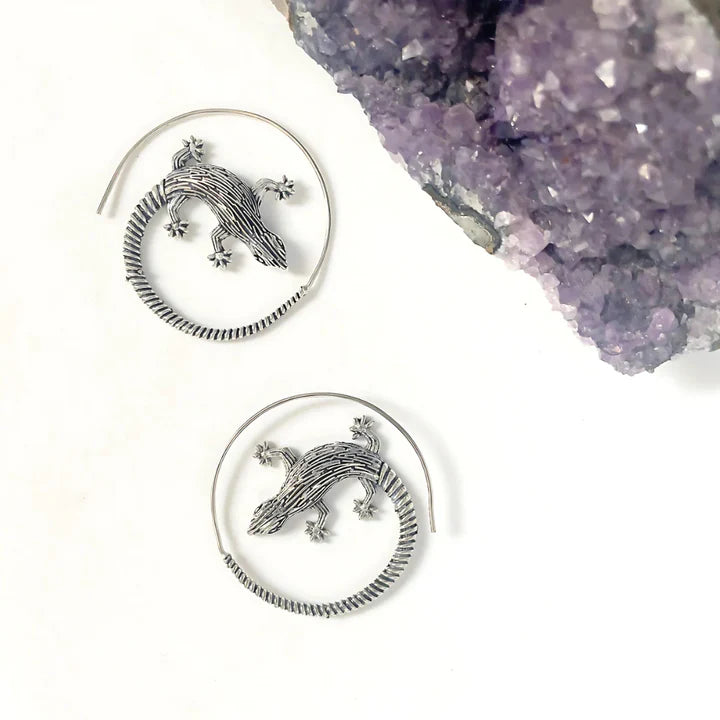 Golden lizard hoop earrings displayed beside crystal stones, bold nature-inspired jewelry.