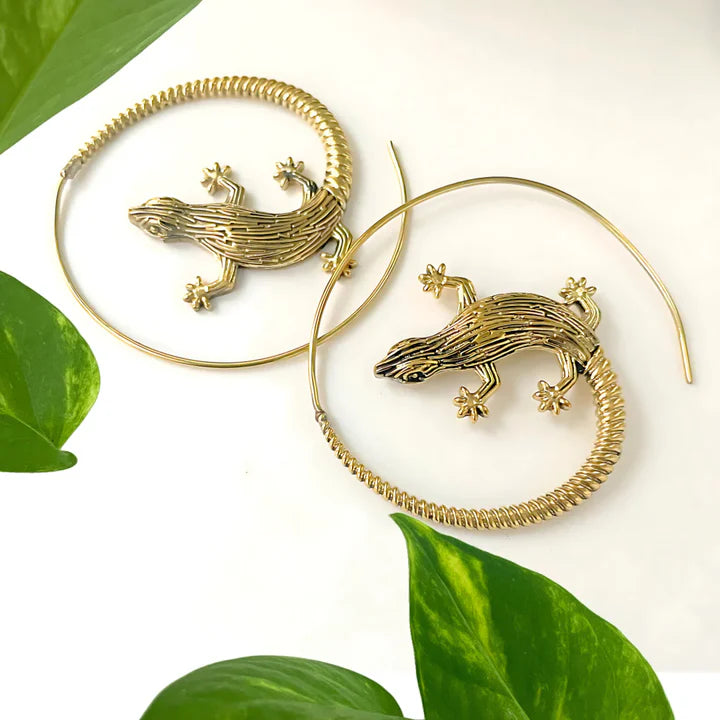 Gold lizard earrings resting on fresh green leaves, elegant boho accessory.