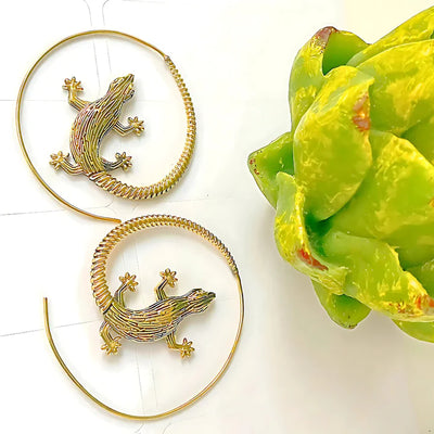 Golden lizard hoop earrings placed on green leaf background, artistic statement accessory.