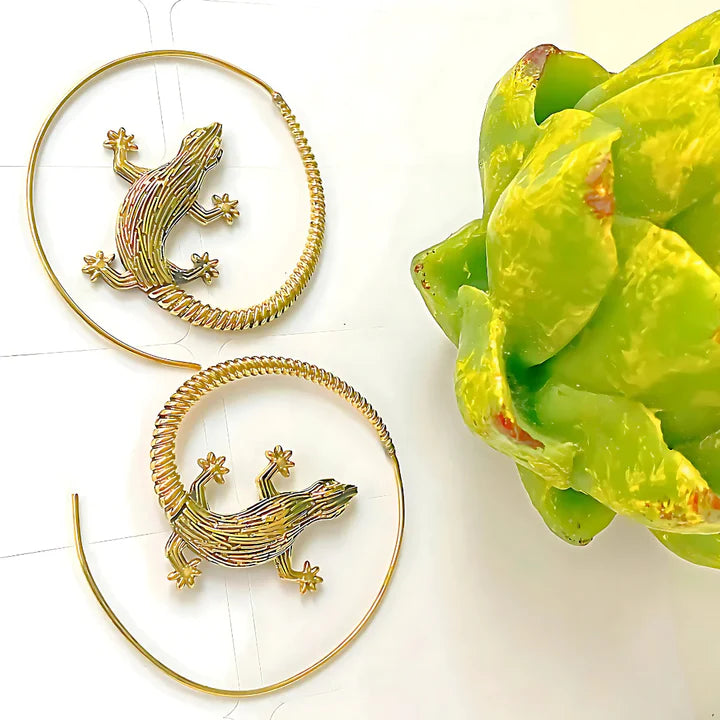 Golden lizard hoop earrings placed on green leaf background, artistic statement accessory.