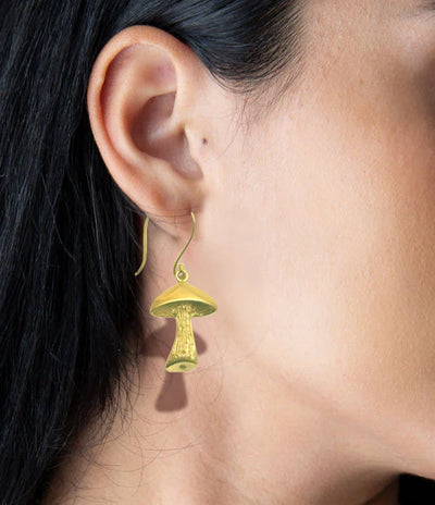 Model wearing golden mushroom drop earrings, modern and playful accessory.