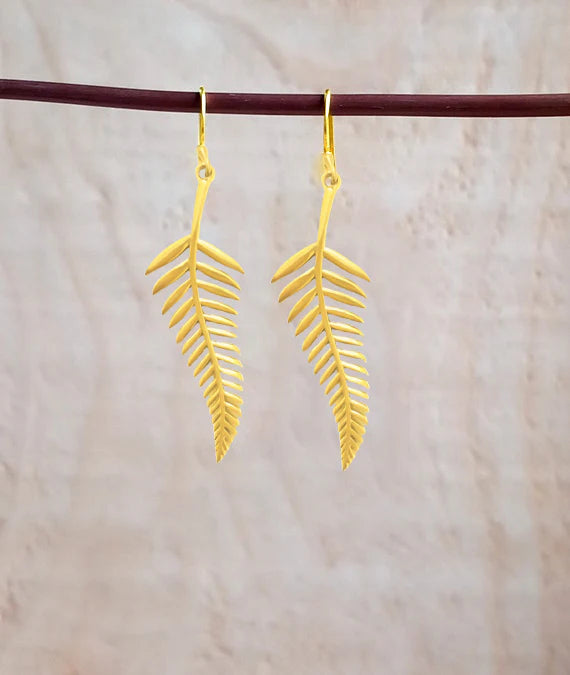 Pair of golden palm leaf earrings hanging on fabric background, elegant handcrafted style.