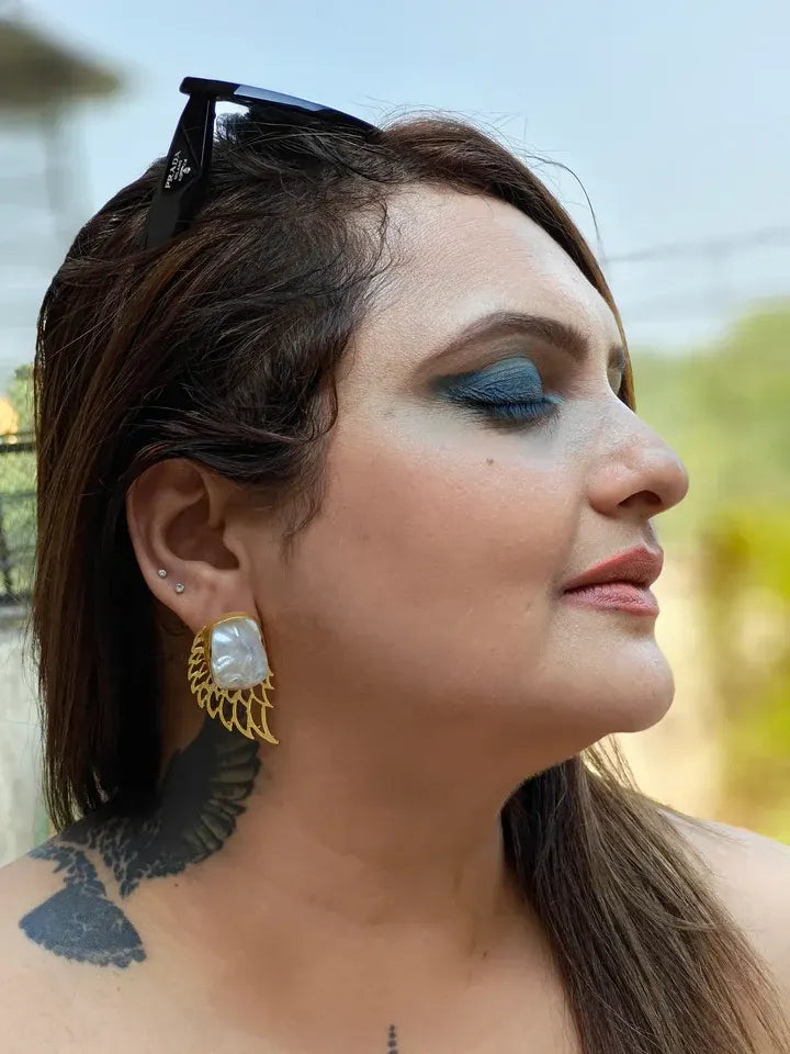 Model wearing golden pearl wing stud earrings, bold angel-inspired fashion accessory.