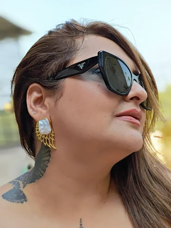 Model wearing golden pearl wing earrings outdoors, luxury handcrafted statement look.