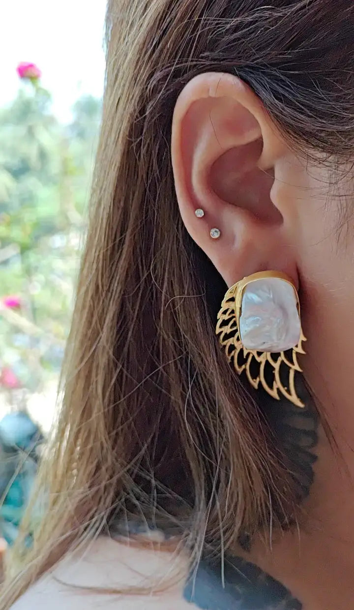 Side view of model wearing golden pearl wing earrings, radiant modern jewelry design.
