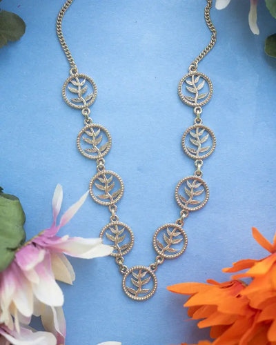 Golden tree of life necklace displayed on blue background with flowers, nature-inspired design.