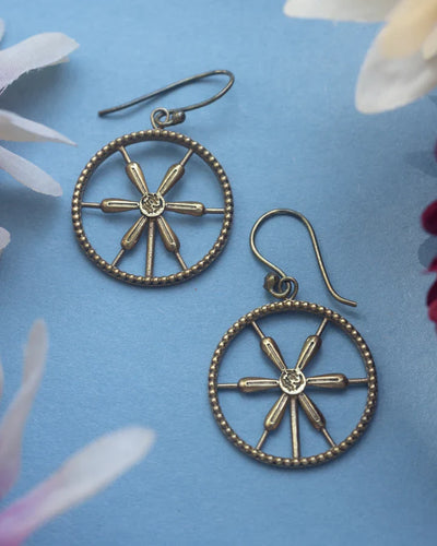 Flat lay of golden wheel spoke earrings on blue floral background, artistic jewelry shot.