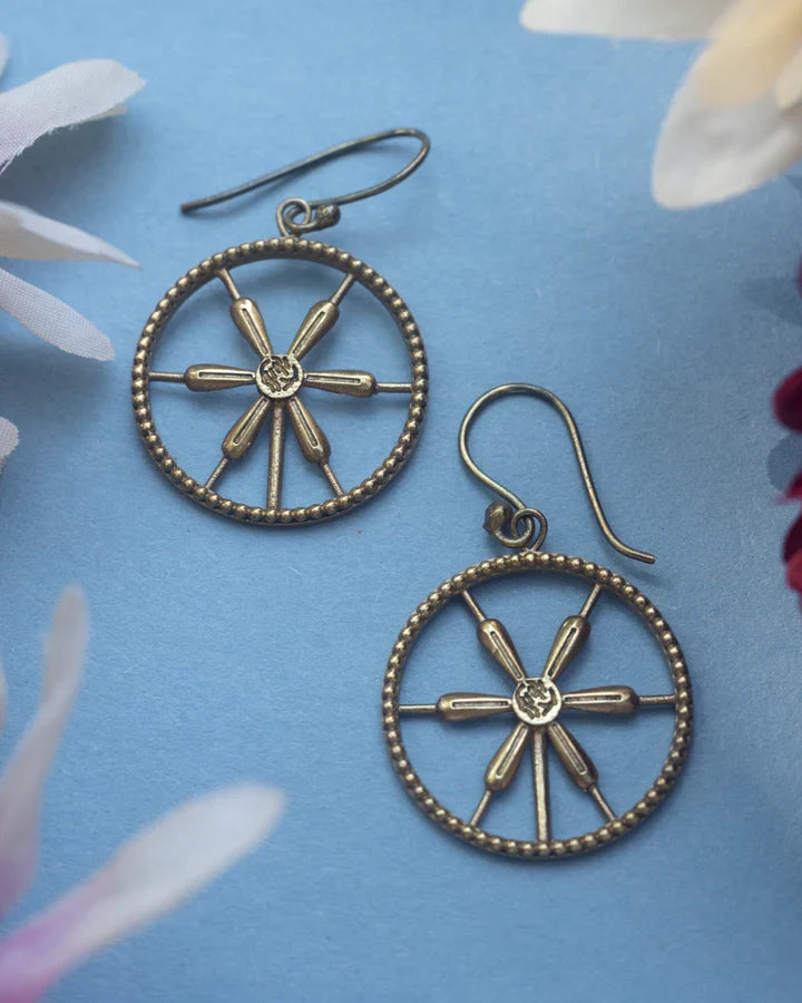 Flat lay of golden wheel spoke earrings on blue floral background, artistic jewelry shot.
