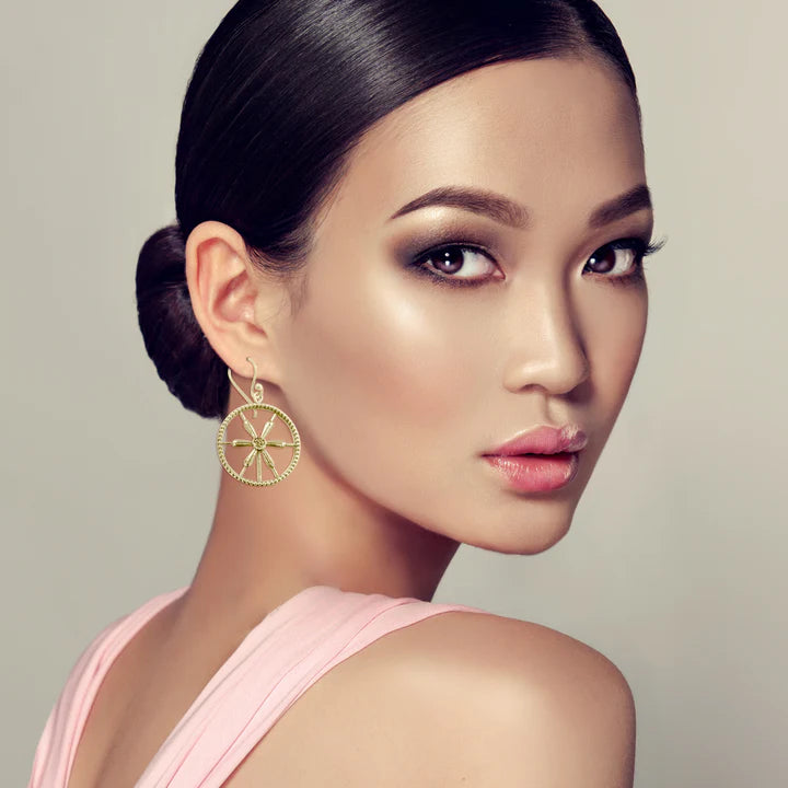 Model wearing golden wheel spoke earrings, elegant circular drop fashion accessory.