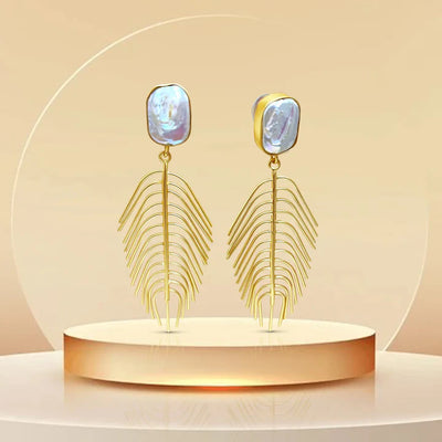 Iridescent pearl and gold leaf drop earrings displayed on podium, statement jewelry design.